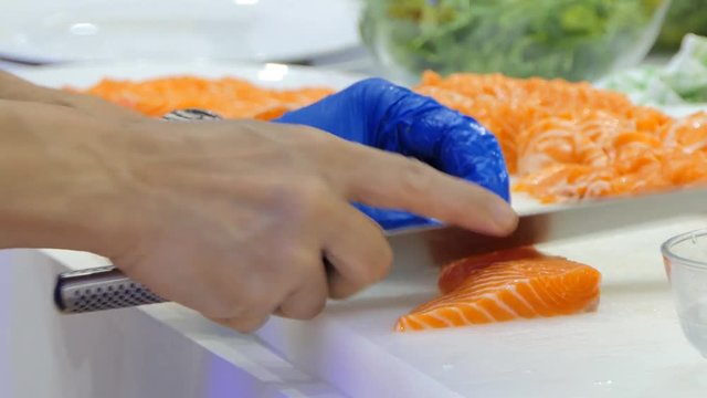 Chef using knife slice raw salmon on chopping board.