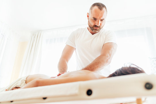 Bearded Masseur making a therapeutic back massage for a girl lying on a massage couch in a massage spa.