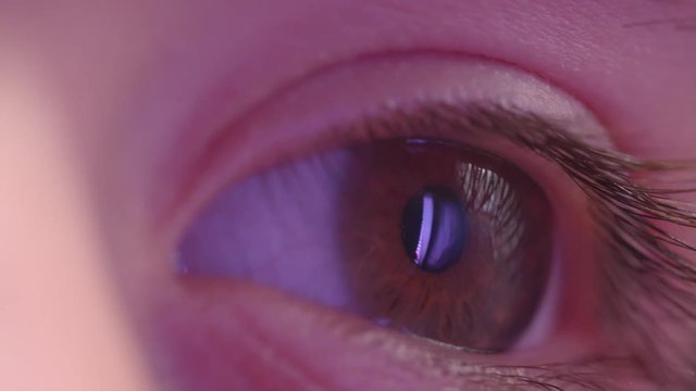 Close-up shoot of l eye watching rightwards with reflection of violet lamp in it.