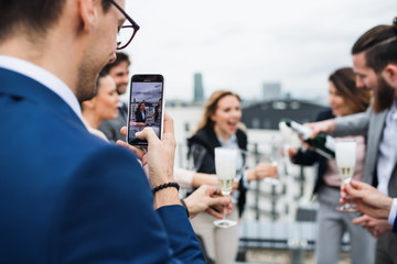 A group of joyful businesspeople having a party outdoors on roof terrace in city. - obrazy, fototapety, plakaty