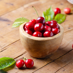 Fresh ripe cherries in wooden bowl on rustic table.