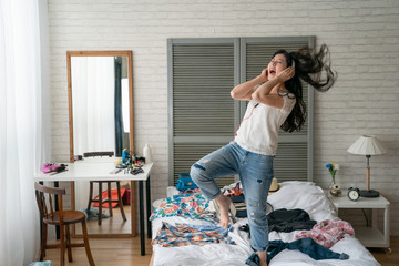 Excited woman listening to music and dancing in home bedroom. crazy funny girl wear headphones enjoy melody new songs on internet move body relax while packing prepared luggage with clothes on bed.