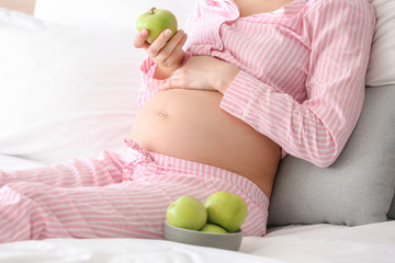 Young pregnant woman with apples in bedroom