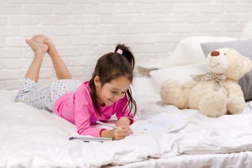 cute little girl drawing pictures while lying on bed. Kid painting at home