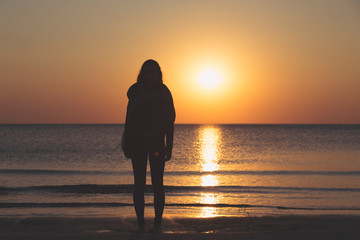 sunset over the sea, silhouette of a woman standing on the beach