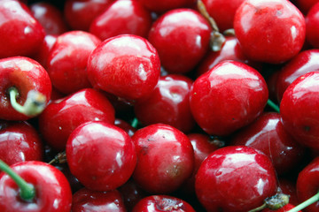 Close up of a pile of ripe cherries with stalks and leaves. A large collection of fresh red cherries. Ripe cherry background. Close-up.