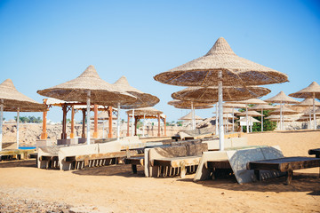 A row of straw umbrellas to protect against overheating on a sandy beach against a blue sky and blue sea. The concept of summer holidays, tourism, travel.