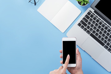 Woman holding smartphone with a minimal blue desk, concept of online shopping, internet payment, e-commerce, copy space, flat lay, top view, mock up