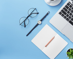Girl write on open white book or accounting on a minimal clean light blue desk with laptop and accessories, copy space, flat lay, top view, mock up