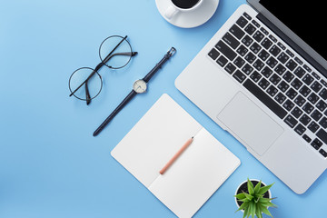 Girl write on open white book or accounting on a minimal clean light blue desk with laptop and accessories, copy space, flat lay, top view, mock up