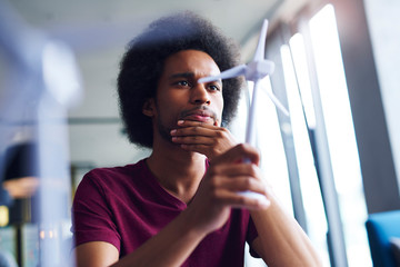 Focused African man looking at model of wind turbine