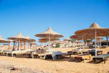 A row of straw umbrellas to protect against overheating on a sandy beach against a blue sky and blue sea. The concept of summer holidays, tourism, travel.