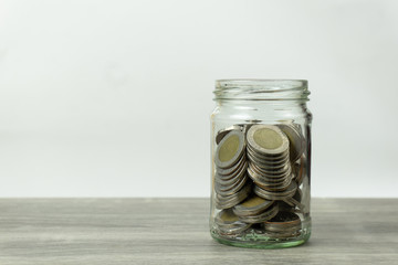 Saving money concepts. Stacked coins in glass jar on wooden table with white background.