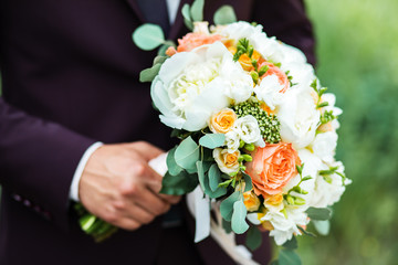 A beautiful bouquet of mixed flowers in the hand of the groom in a suit. Wedding bouquet of fresh flowers for the bride