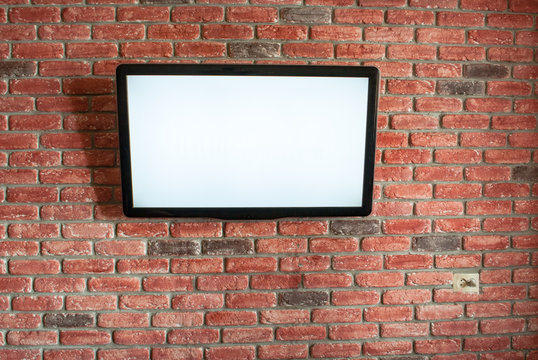 On the red interior brick wall is a white screen TV