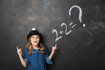 Young little school girl posing isolated over chalkboard wall background.