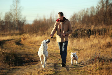 Young happy european smiling and laughing walking in a field with two dogs