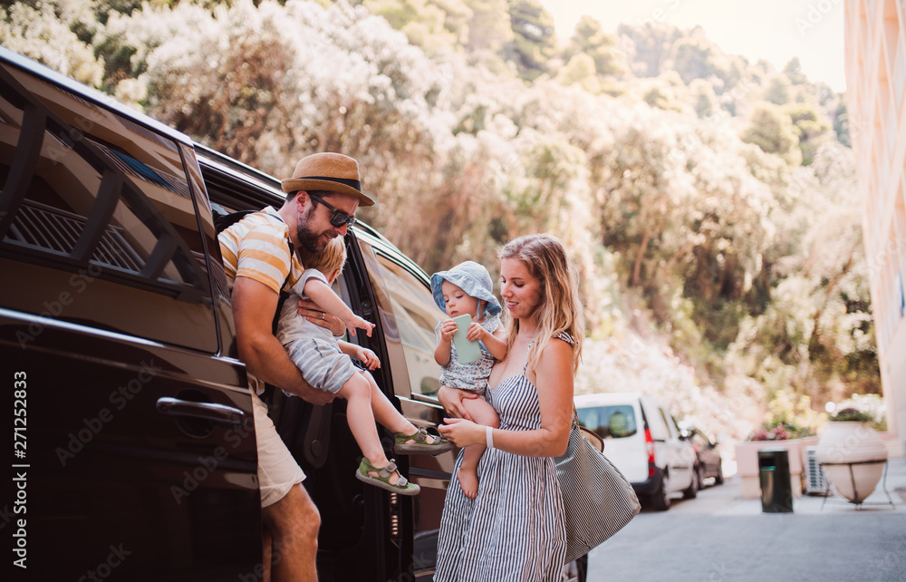 Wall mural A young family with two toddler children getting out of taxi on summer holiday.