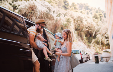 A young family with two toddler children getting out of taxi on summer holiday.