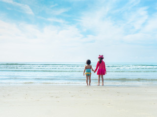 Two little girls are standing and hand to hand at the beach and sea. Older sister holding hand younger sister to play at the beach and sea.