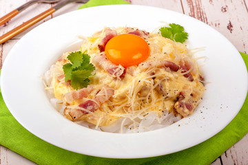 Traditional dish of Italian cuisine carbonara sauce with low-carb shirataka paste and egg yolk. Large portion served on a white plate. Close up and horizontal view.