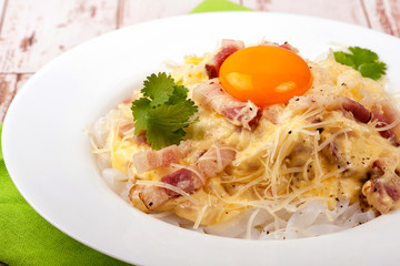 Traditional dish of Italian cuisine carbonara sauce with low-carb shirataka paste and egg yolk. Large portion served on a white plate. Close up and horizontal view.