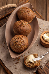 Low-carb gluten-free buns baked with coriander seeds. Served with butter on a wooden tray and a natural rustic napkin. Close up and vertical view.