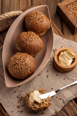 Low-carb gluten-free buns baked with coriander seeds. Served with butter on a wooden tray and a natural rustic napkin. Close up and vertical view.