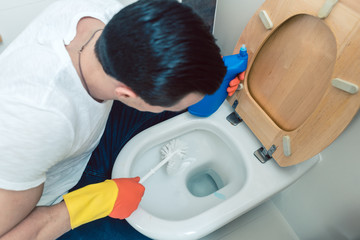 Mann ekelt sich ein bisschen vom Reinigen der Toilette