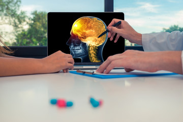 Doctor showing a x-ray of skull with pain in front of the brain on a laptop to a woman patient. Headache migraine concept