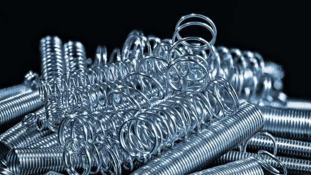 Elastic stainless steel coil springs. Helical wire winding detail. Abstract pile of shiny compression and extension metal parts on black background. Springy machine components. Mechanical engineering.