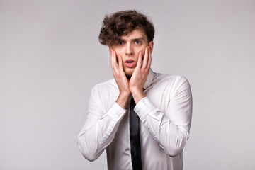 Portrait of young man with shocked emotional facial expression and hands gesture over light gray background