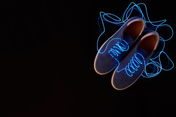 Top view of a pair of suede sneakers with neon laces on black background