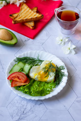 Fried eggs with lettuce, cucumber and tomato slices on a light background