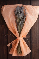 Lavender flowers in a paper on a brown wooden background. 