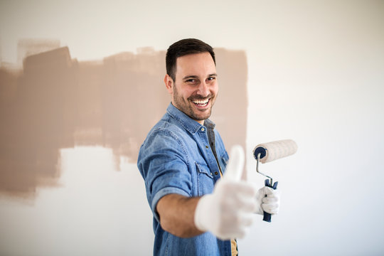 Handsome man painting walls with roller.