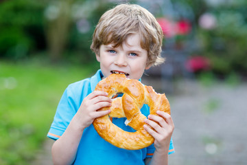 Adorable little kid boy eating huge big bavarian german pretzel.