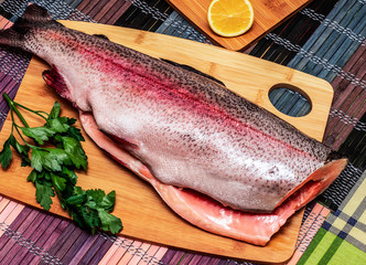 Fresh red fish with greens and lemon on a wooden board. Horizontal orientation