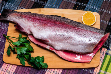 Fresh red fish with greens and lemon on a wooden board. Horizontal orientation