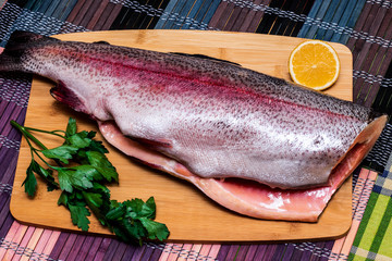 Fresh red fish with greens and lemon on a wooden board. Horizontal orientation