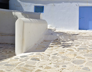 White house with blue windows and stone paved yard, empty space, Tinos island, Greece.