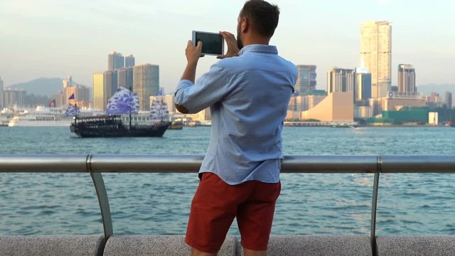 Young, happy man taking photo with tablet computer of Hong Kong skyline
