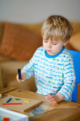 Cute toddler boy playing with wooden hammer tool at home in workshop. Kid boy play as handyman....