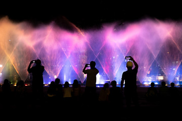 Fototapeta na wymiar Abstract silhouette of crowd taking photo by camera smartphone for capture moment on the light and music fountain show. Silhouette Concept.