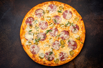 Homemade pizza with salami, mozzarella and pickles. Top view on dark stone table