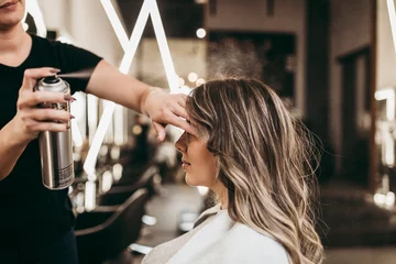 Fototapete Beautiful young woman with long curly hair in hair salon. Professional hairdresser styling with hairspray. © Dusko