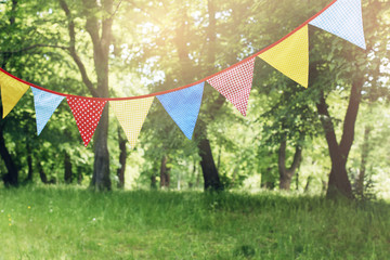 Colorful bunting flags hanging in park. Summer garden party. Outdoor birthday, wedding decoration....