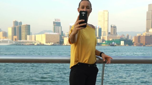 Young, happy woman taking selfie photo with cellphone in Hong Kong city