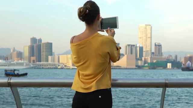 Young woman taking photo with tablet computer of Hong Kong skyline