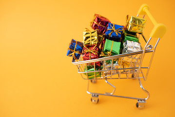 Christmas gifts in a supermarket trolley on yellow background. Online shopping concept - trolley full of gifts. Black Friday and Cyber Monday